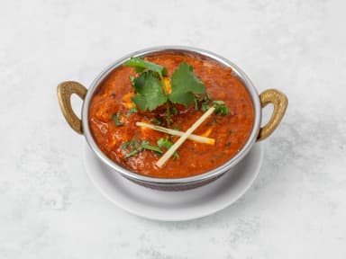Chicken curry in a steel karahi bowl, garnished with coriander and ginger strips