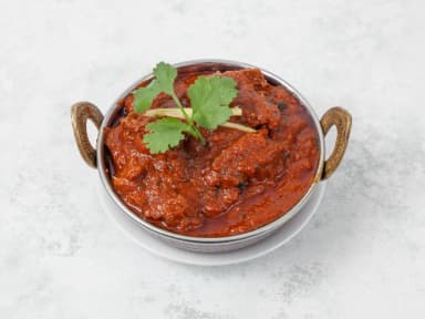 Lamb curry in a steel karahi bowl, garnished with coriander