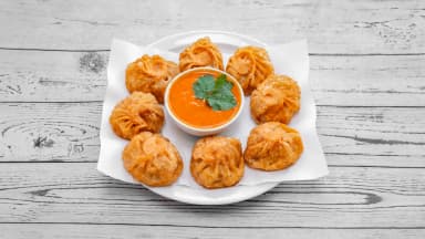 Fried lamb momos on paper with a bowl of orange dipping sauce